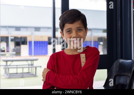 Biracial boy with a bright smile, wearing a red shirt, stands confidently at school Stock Photo