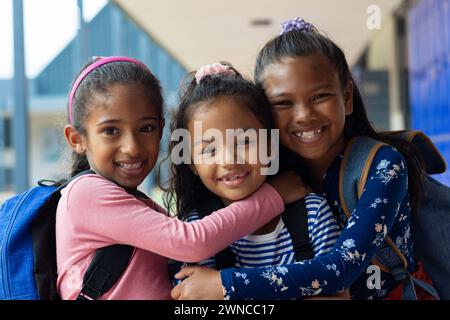 Three biracial girls are smiling and embracing in a school setting Stock Photo