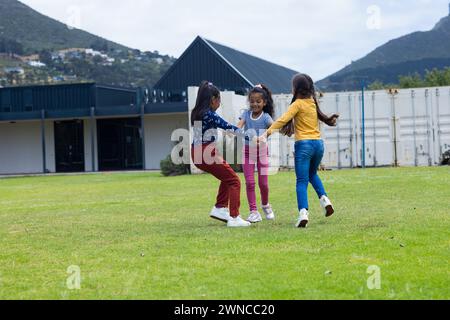 Three girls are playing and holding hands in a grassy outdoor area in school Stock Photo