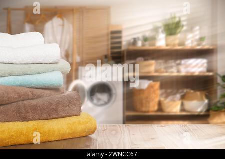 Folded clean towels on wooden table in laundry room, space for text Stock Photo