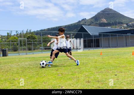 Biracial boy and African American boy play soccer outdoors in school Stock Photo