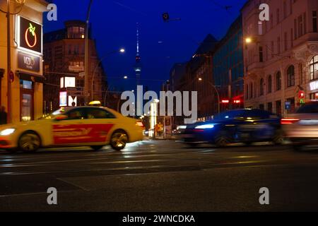 Cars driving down night Oranienburger street, Illuminated buildings and Fernsehturm TV tower visible in background, Nightlife, sustainability and envi Stock Photo