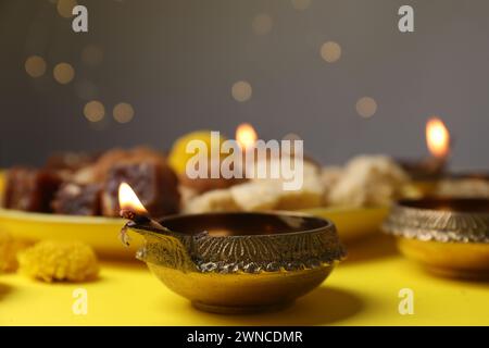 Happy Diwali. Diya lamp on yellow table against blurred lights, closeup Stock Photo