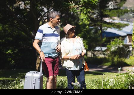 Senior biracial couple enjoys a sunny day outdoors with luggage in tow Stock Photo