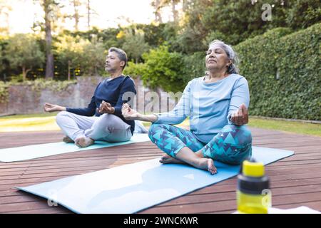 Senior biracial woman and biracial man practice yoga outdoors at home Stock Photo