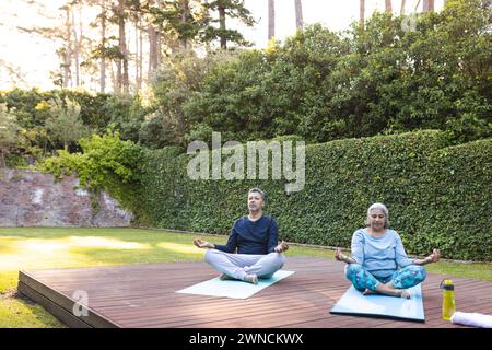 Senior biracial woman and biracial man practice yoga outdoors with copy space at home Stock Photo