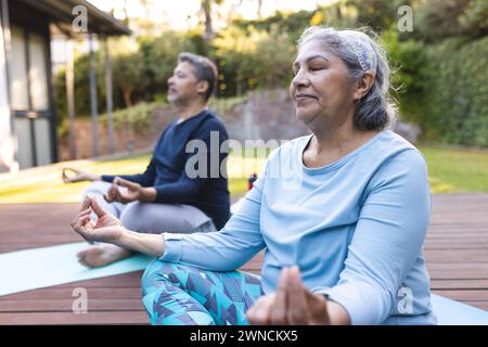 Senior biracial woman and man meditate in a serene garden setting at home Stock Photo