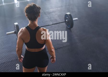 A young strong fit biracial woman stands ready before a barbell in a gym with copy space Stock Photo