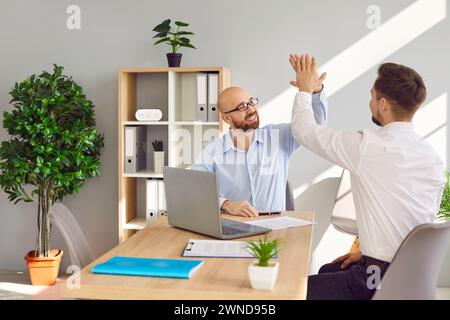 Two friendly male colleagues compliting task and giving high five Stock Photo