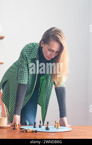 Vertical composition. Portrait of a woman stands with her hands on the table and looks intently at the chess pieces on the blue circle. Psychological Stock Photo