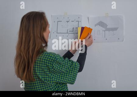 Adult Woman Choosing Color For Small House Whose Project Is Attached To Wall. Back view Stock Photo
