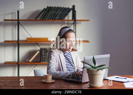 A young pretty lady is working thoughtfully and intently at her laptop. Stock Photo