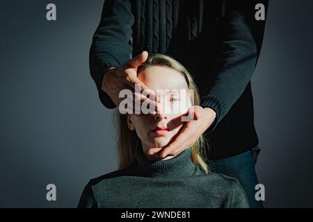 Visualization of a psychological problem. Difficulties in mutual understanding. A man holds the head of an adult young woman in his hands, closing one Stock Photo