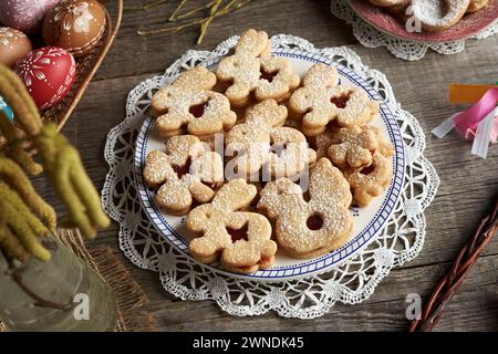 Homemade Linzer cookies in the shape of cute animals, with Easter eggs decorated with wax in the background Stock Photo