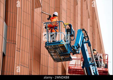 Construction workers on raised platforms putting finishing touches to windows Stock Photo
