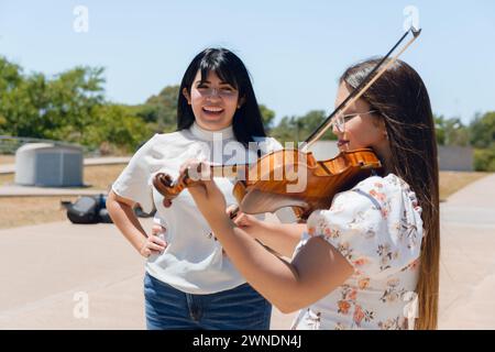 group of young latin women artist singer and violinist busker, on street working making music at noon, in buenos aires argentina. Stock Photo