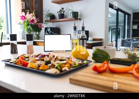 A tablet with a blank screen stands among various cooking ingredients on a kitchen counter Stock Photo