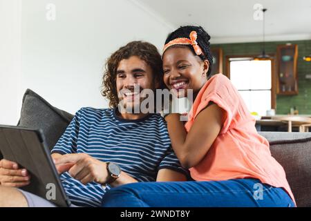 Diverse couple young African American woman and Caucasian man share a tablet, smiling together Stock Photo