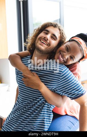 Diverse couple young African American woman embraces a young Caucasian man from behind, both smiling Stock Photo