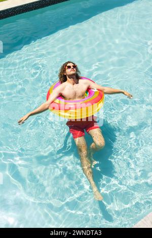 Young Caucasian man with curly hair relaxes on a colorful float in a pool with copy space Stock Photo