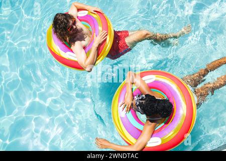 A diverse couple, a young Caucasian man and an African American woman relax on colorful pool floats Stock Photo