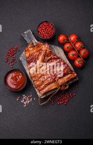 Delicious smoked or grilled ribs with olives, spices and herbs on a dark concrete background Stock Photo