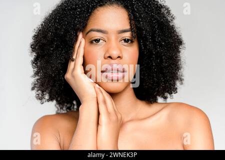 A close-up portrait of an African-American woman, her hand delicately framing her face, reveals a compelling gaze and an air of reflective thoughtfulness, set against a neutral background. Stock Photo
