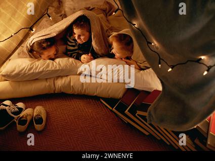 Kids, happy and sleepover in tent at night with conversation, bonding and holiday adventure or vacation. Funny friends or children by fairy lights Stock Photo