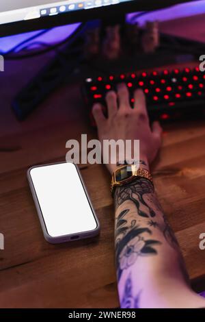 Hands of a tattooed man typing on an RGB keyboard with copy space. Stock Photo
