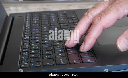 A close-up view of a senior mans hands as he types on a laptop located on a kitchen countertop. Natural light fills the room Stock Photo