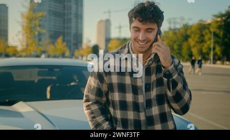 Handsome smiling Caucasian man happy businessman 30s guy male driver rent car in city talk mobile phone pleasant conversation talk with friend Stock Photo