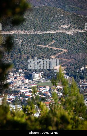 Beautiful mountain view through the trees over the city of Budva in winter. Zigzag road up. Vertical. Europe, Budva, Montenegro. Stock Photo