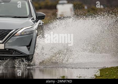 Water spray from a car wheel and the front section of the car as it drives through a flooded road Stock Photo