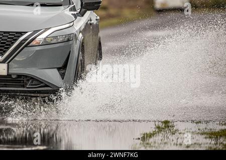 Water spray from a car wheel and the front section of the car as it drives through a flooded road Stock Photo