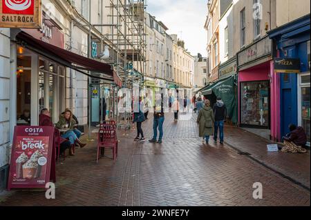 Teignmouth town centre shopping street with a Costa coffee cafe, pedestrians and a homeless person on the pavement. Stock Photo