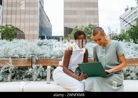two businesswomen working with laptop and talking in park Stock Photo