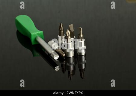 Screwdriver bits of different sizes and the screwdriver itself lie on a dark background. Stock Photo