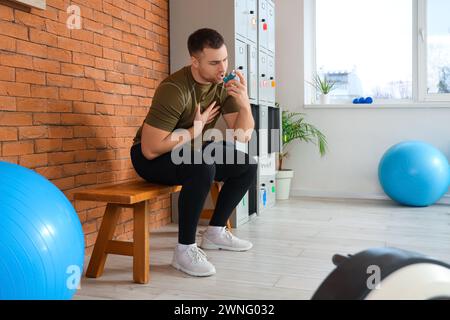 Sporty young man using inhaler on bench in gym Stock Photo