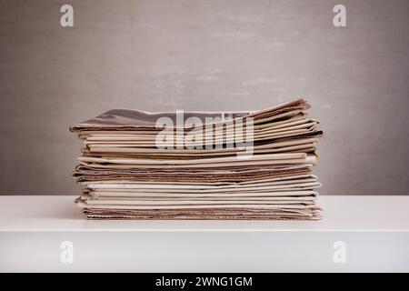 a stack of newspapers on a white table on a grey background Stock Photo