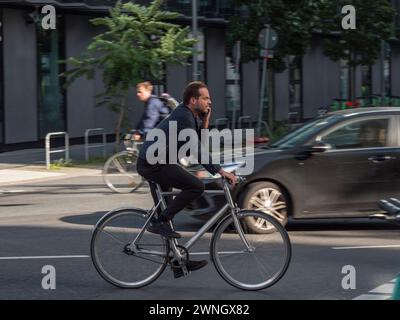 A cyclist riding down the road while holding a mobile phone to his ear, Berlin, Germany. Stock Photo