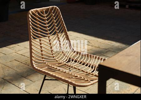 Rattan chair illuminated by sunlight, highlighting its elegant and artisanal design, ideal for modern interiors and outdoor spaces. Stock Photo