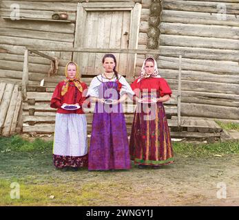 Young Russian peasant women in front of traditional wooden house, in a rural area along the Sheksna River near the small town of Kirillov. Early color photograph from Russia, created by Sergei Mikhailovich Prokudin-Gorskii as part of his work to document the Russian Empire.  1909 Stock Photo