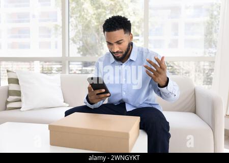 Concerned annoyed young African costumer man using smartphone Stock Photo