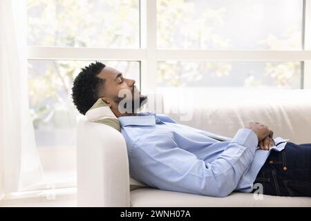 Peaceful calm young African American man lying on white couch Stock Photo