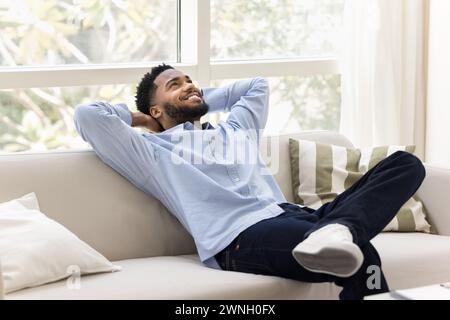 Happy carefree young African man relaxing on cozy home couch Stock Photo