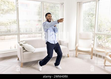 Cheerful overjoyed African man dancing in white colored home interior Stock Photo