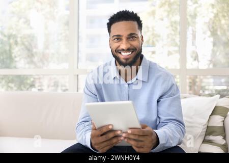 Happy handsome young Black man holding tablet, looking at camera Stock Photo