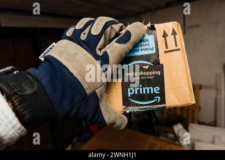 Bremen, Germany - Dec 10, 2023: In a large, dimly lit warehouse, a male hand wearing a glove holds an Amazon Prime cardboard parcel, featuring fast, free delivery as fast as today, with the Whole Foods Market logo displayed on the cardboard Stock Photo