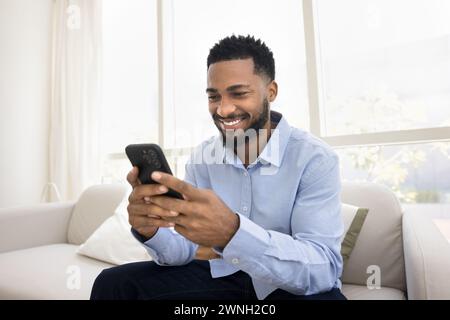 Happy young Black man typing on smartphone with toothy smile Stock Photo