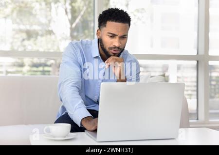 Focused pensive young African freelancer man working at laptop Stock Photo